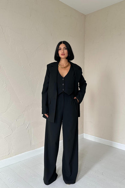 Woman wearing tailored black trio set with blazer, vest, and wide-leg trousers.