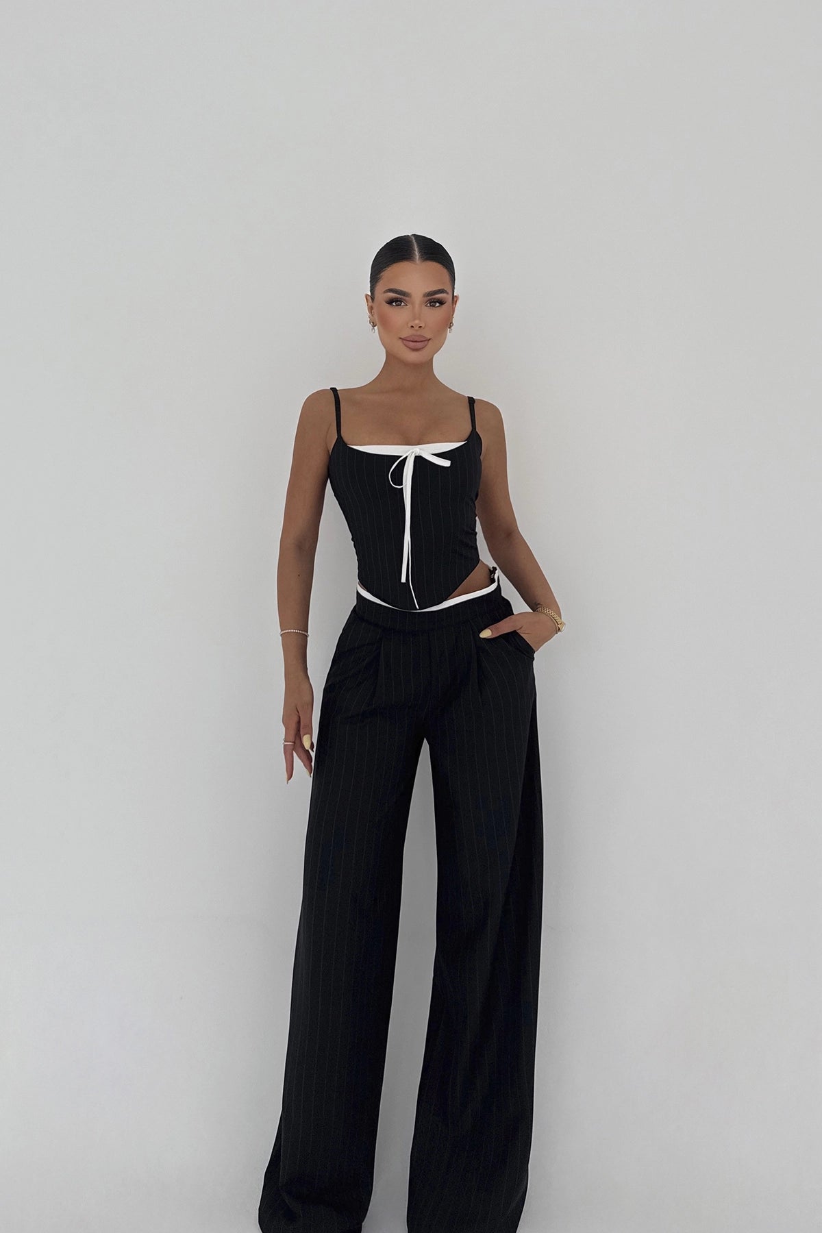 Model wearing black pinstripe cut-out set with corset-style top  and bow detail and wide-leg trousers.
