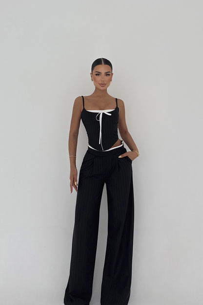 Model wearing black pinstripe cut-out set with corset-style top  and bow detail and wide-leg trousers.
