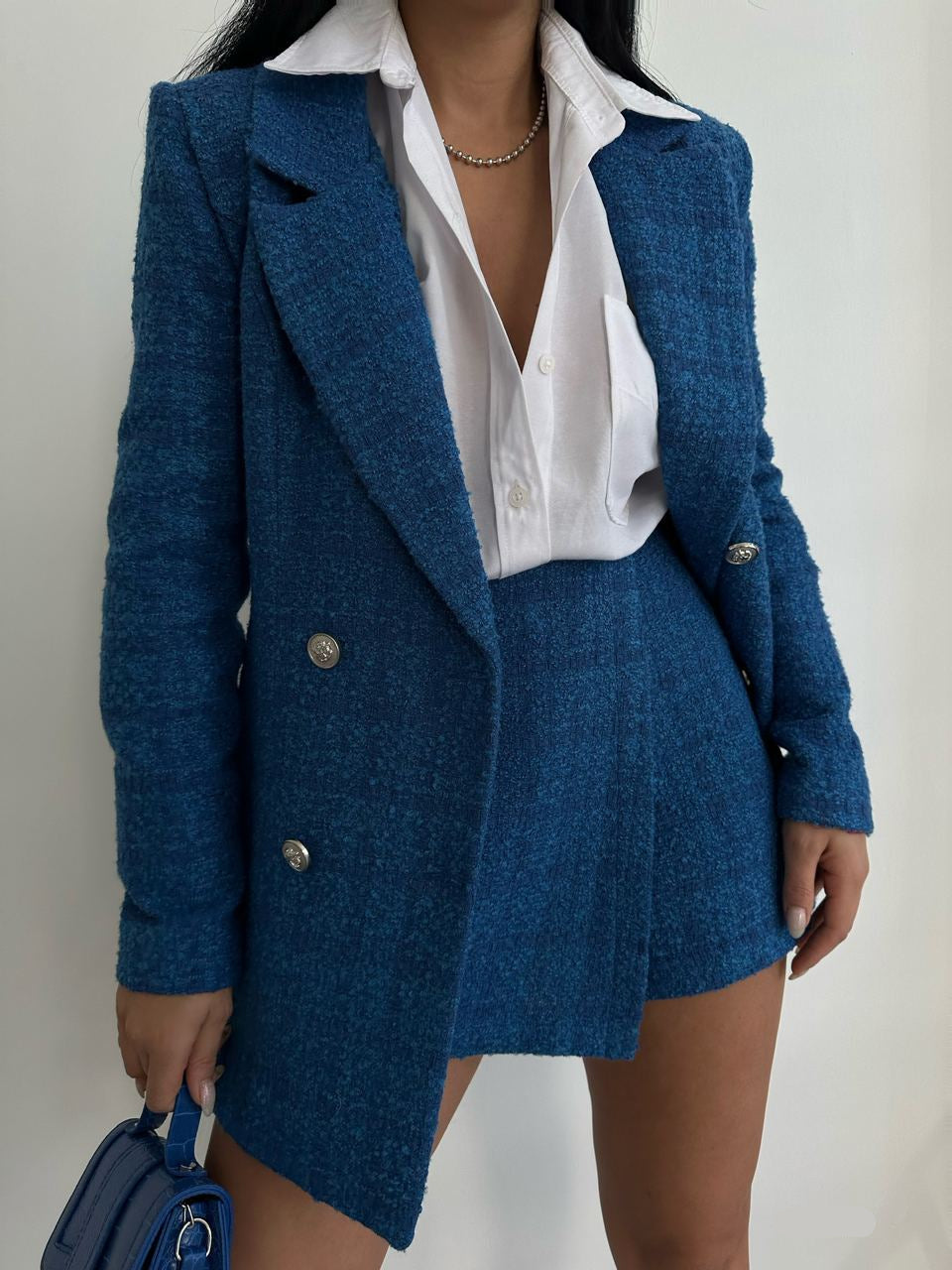 Person wearing a blue blazer and skirt set with a white shirt, holding a blue handbag.