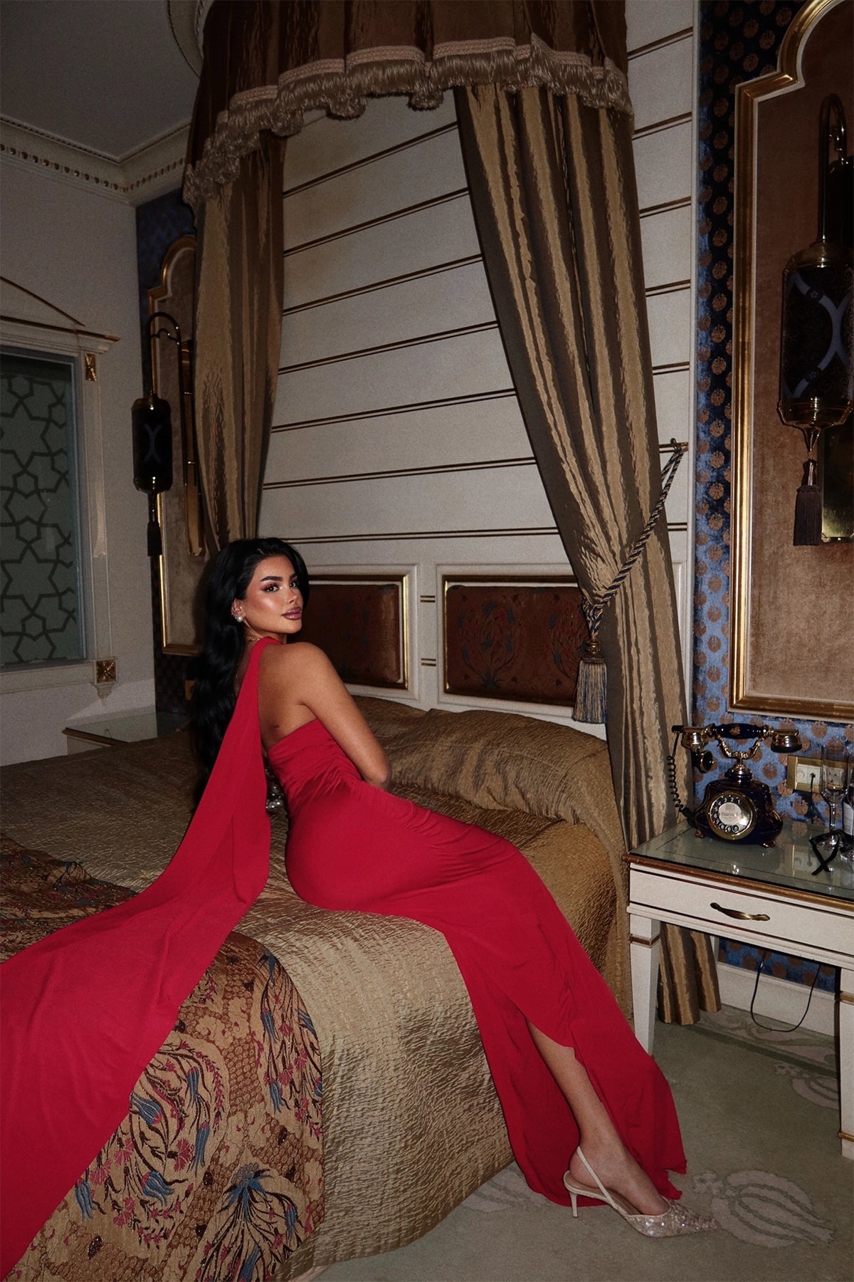 Back view of a floor-length red dress with draped tie detail, styled with nude heels.